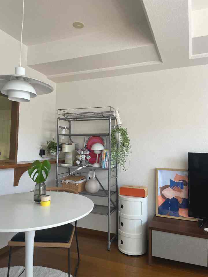 白い壁と茶色の木製床がある2LDKリビング、丸いダイニングテーブルや植物のある棚が配置されたミッドセンチュリーモダン風の印象的な空間