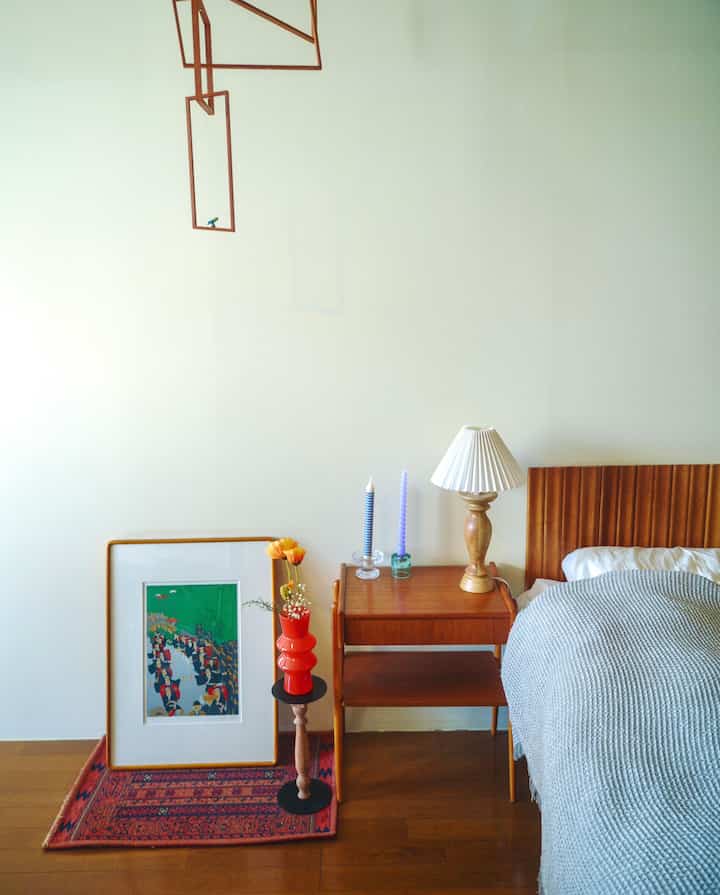 A Nordic-style bedroom with wood-tone flooring and furniture, featuring a gray bedspread and vintage decorative accents