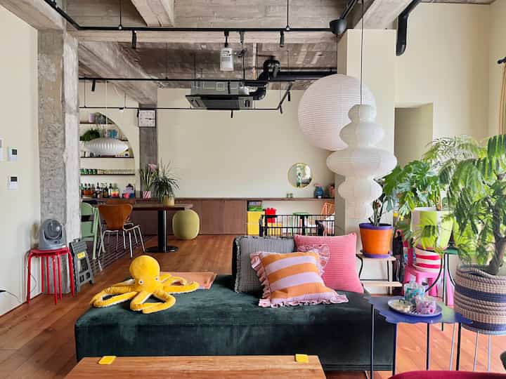 White and brown toned living room featuring green sofa, pink cushions, plants, and pendant lights in a mid-century modern style