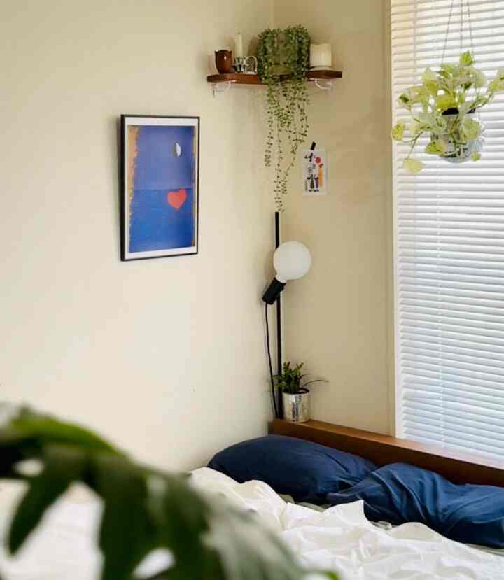 暖かいベージュのトーンの寝室、ネイビーの枕と白い寝具が調和し、モダンな照明と植物が配置された落ち着いた空間