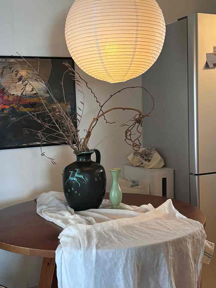 白い照明と木目調の丸いダイニングテーブル、花瓶が配置されたミッドセンチュリーモダンのダイニング空間