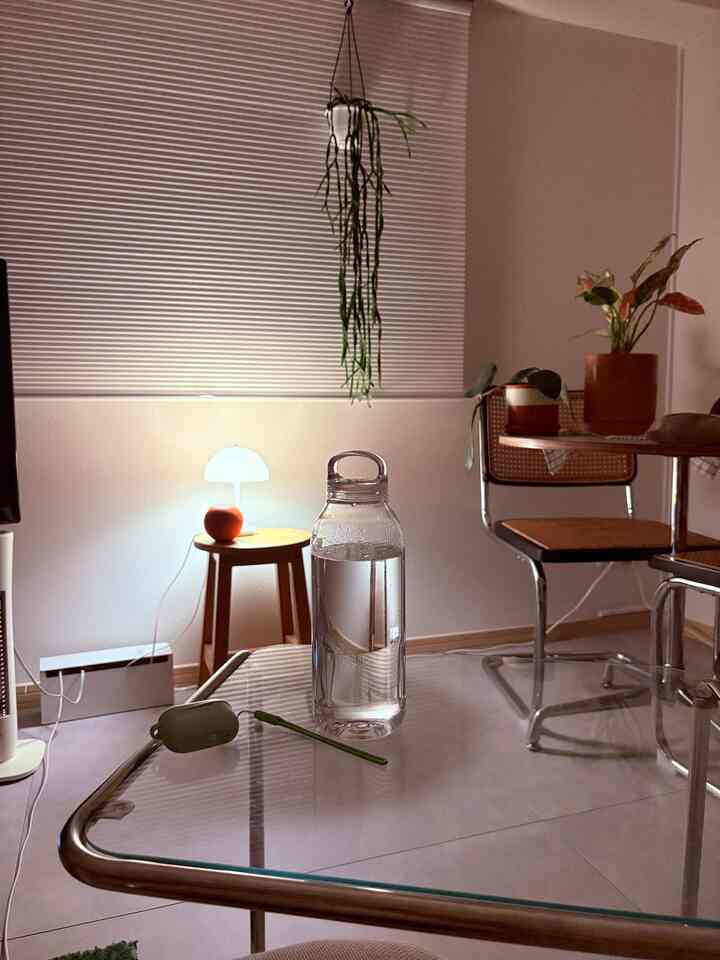 白と木目調の寝室、透明なガラステーブルに水のボトルが置かれ、落ち着いた夜のミッドセンチュリーモダン風インテリア空間