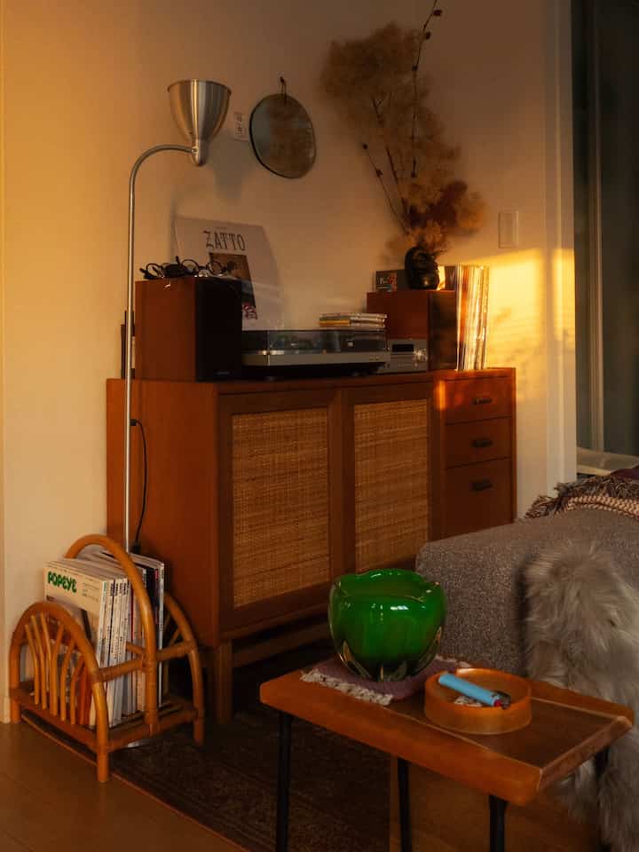 暖かい木目調のミッドセンチュリーモダンリビング、キャビネットとソファ、緑色のガラス花瓶が配置された雰囲気のある空間