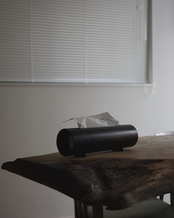 Natural color and wood tone dining room featuring a rustic wooden table with a black objet-like tissue case, creating a simple atmosphere