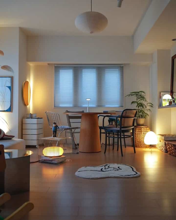 Natural modern dining room in white and brown tones featuring a round table, armchairs, and warm ambient floor and table lamps