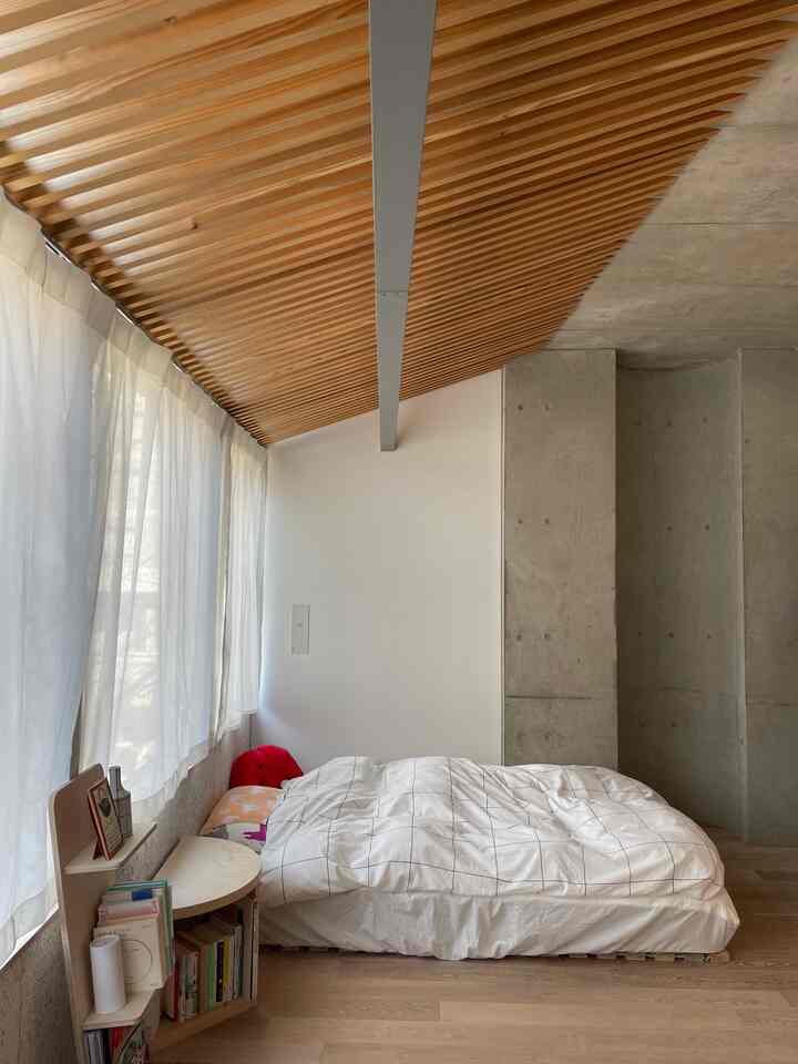 ナチュラルな木目調のスラット天井が特徴的なコンパクトな寝室、白と青のチェック柄掛け布団カバーが配置された落ち着いた空間