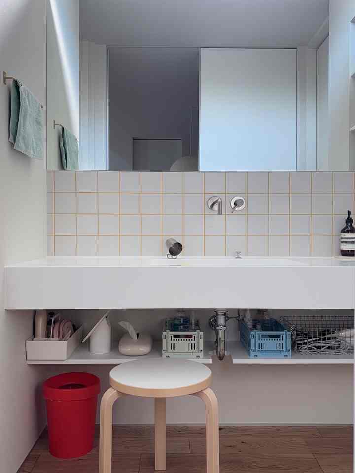 白と木目調のシンプルなバスルーム、使いやすい収納とスツールが配置された化粧台空間