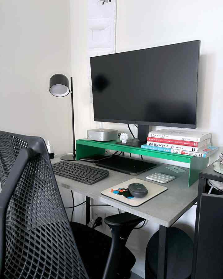 An 8-tatami sized studio workspace with white walls and gray desk, featuring a black mesh chair and green monitor stand in a neat, modern home office setup