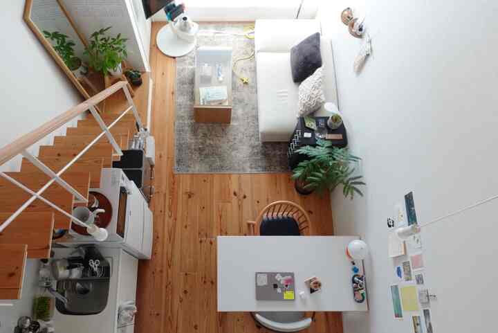 ナチュラルな木目調の床と白い壁のロフト付きワンルーム、ソファとラグのあるリビングスペースとデスクとチェアのワークスペースが分かれた居心地の良い空間