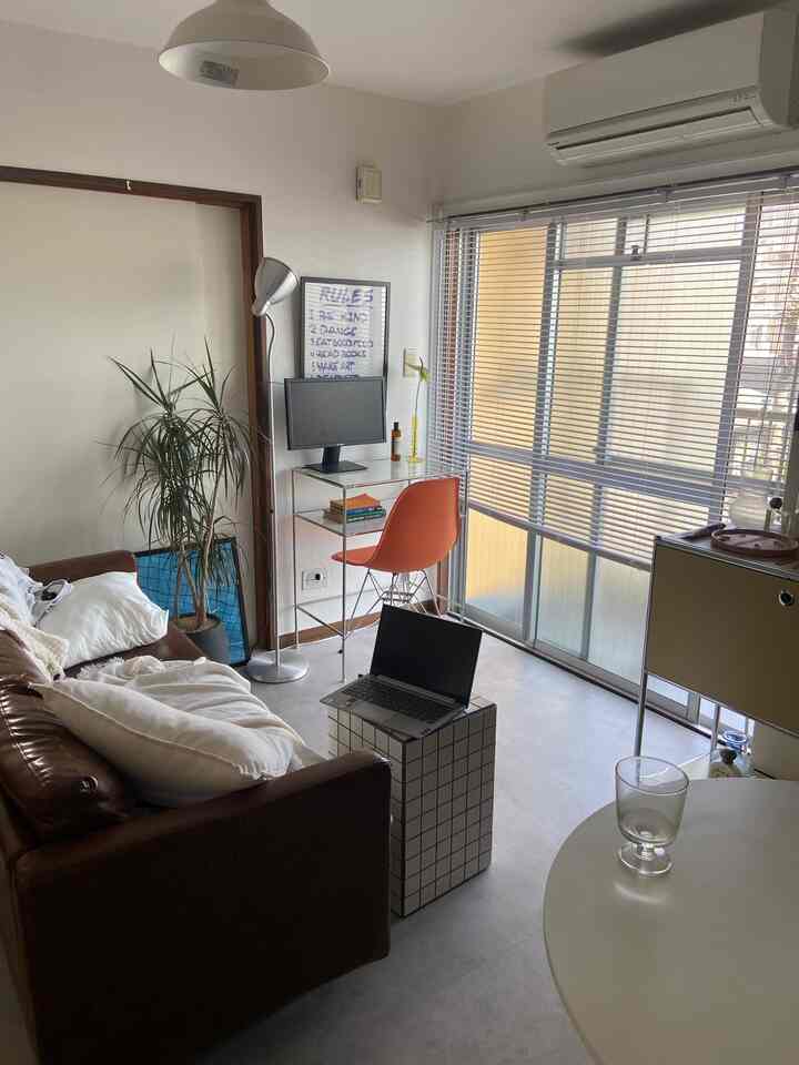 Modern compact home office with white walls and brown leather sofa, featuring an orange chair and modular desk setup