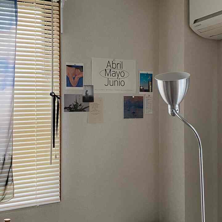 Beige-toned living room corner with blinds, featuring posters on the wall and a metallic floor lamp for a cozy atmosphere