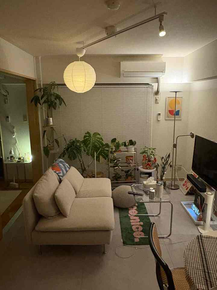 柔らかなベージュの色調のリビング、広いソファとペンダントライト、多様な植物が配置された雰囲気のあるインテリア