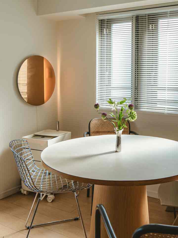 白と木目調が調和するダイニング、丸いダイニングテーブルと花瓶が配置されたシンプルでナチュラルな印象的な空間