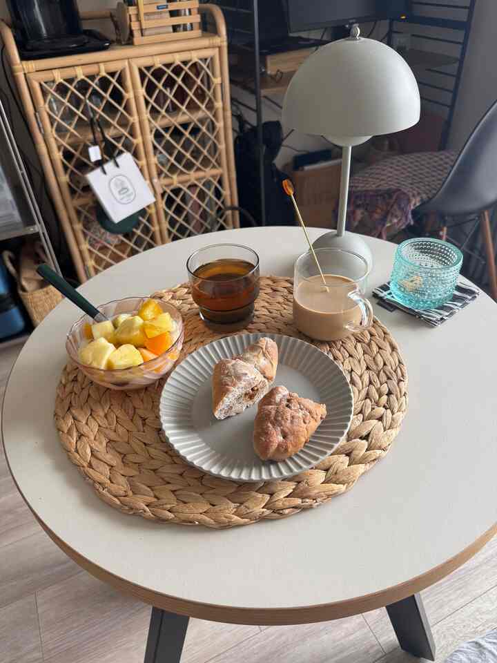 White and natural tone dining room featuring rattan storage cabinet and breakfast setup on table in cozy atmosphere