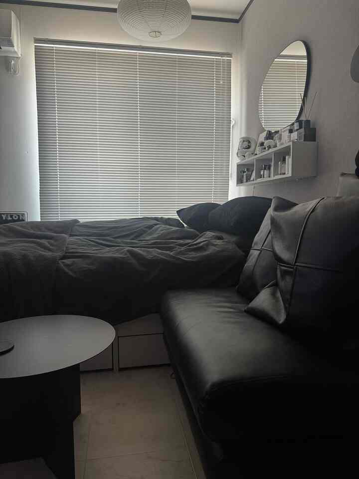 モノトーンの寝室、ブラインド付きの窓、黒いレザーソファとベッドが配置されたモダンで清潔感のあるインテリア