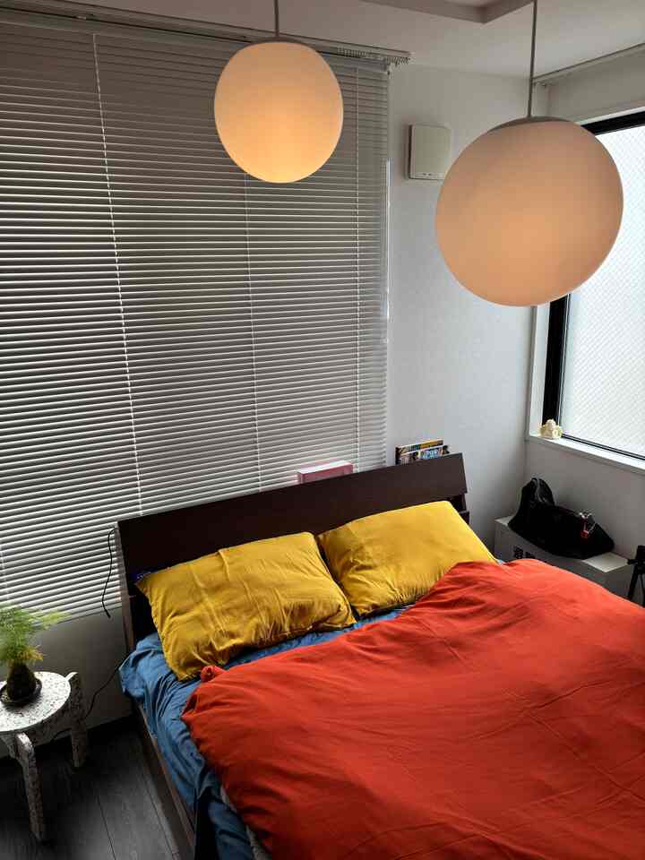 A bedroom with vibrant orange and yellow bedding, wooden bed frame, and white blinds creating a calm atmosphere