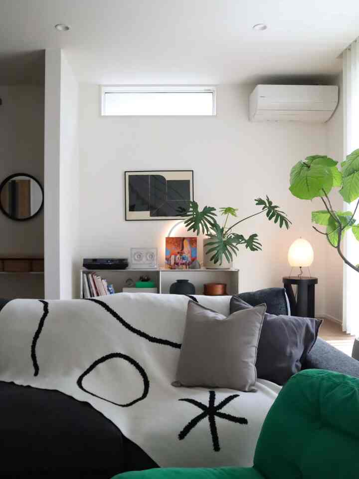 Modern living room with white walls and natural wood floor, featuring a black sofa, green plants and cozy atmosphere