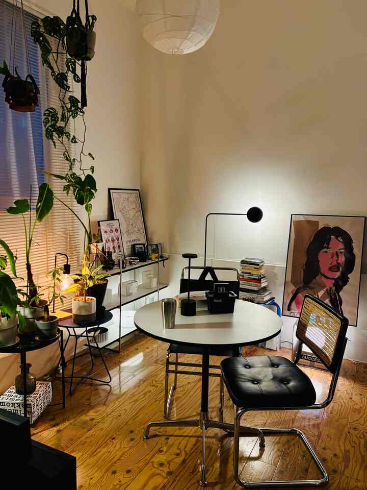 Mid-century modern living room with white walls and wood flooring, featuring a round dining table, chairs, a poster, and greenery creating a cozy atmosphere