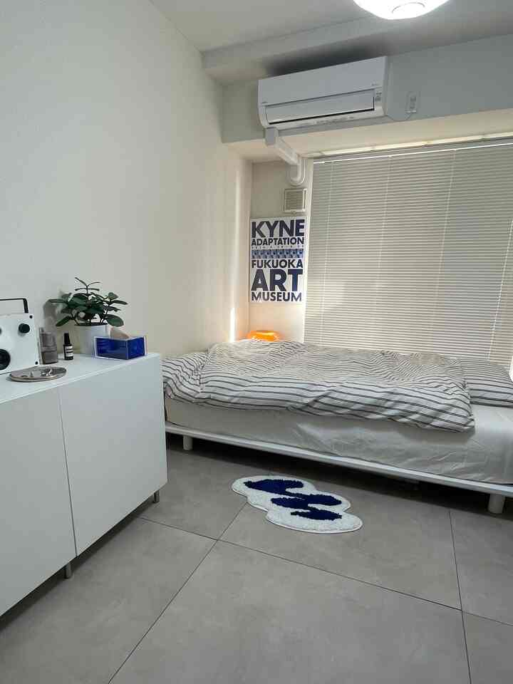 白とグレーのトーンの狭い1K寝室、中央にベッドとブラインドが配置されたシンプルでモダンなインテリア