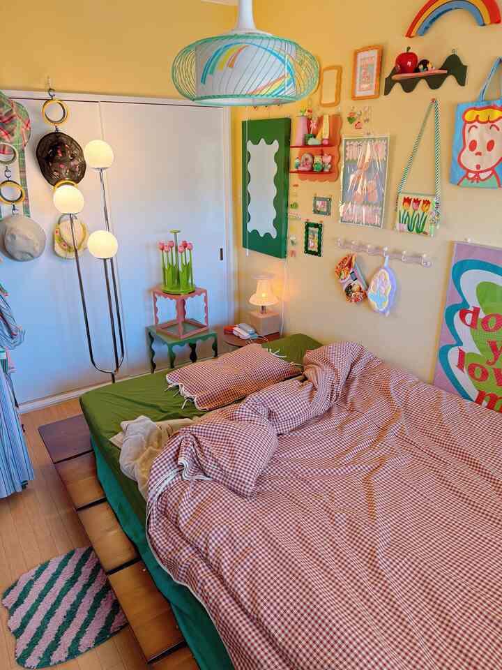 Cozy bedroom with warm yellow walls and natural wooden floor featuring a large bed and colorful wall decor