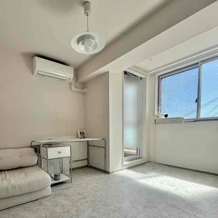 白を基調としたミニマルなリビング、左側にソファとメタルフレームのデスクが配置された明るく清潔感のあるインテリア