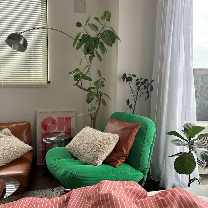 茶色のソファと緑のアームチェアが配置された8畳のワンルームリビング、複数の植物が自然な雰囲気を醸し出すインテリア