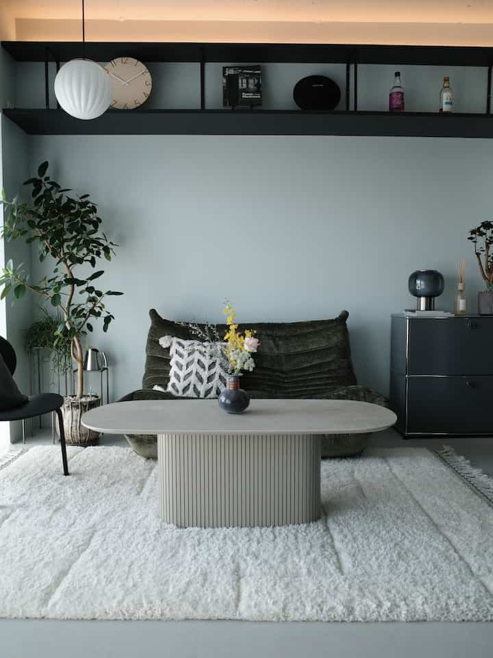 ホワイトカーペットとグリーンソファが配置されたモダンなリビング、植物とコーヒーテーブルが調和する落ち着いたインテリア