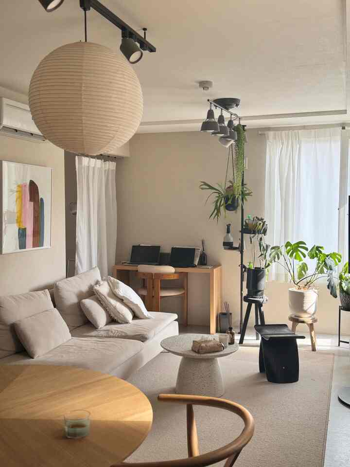 白とベージュのナチュラルな色調の2LDKリビング、ソファやコーヒーテーブル、ホームオフィスデスク、植物が配置された雰囲気のあるインテリア