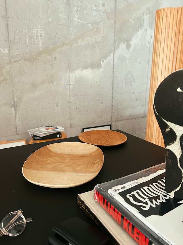 ナチュラルトーンの木製皿と黒いダイニングテーブル、コンクリートの壁が調和したモダンなリビング空間