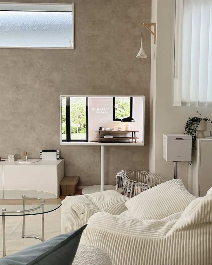 Natural tone wall living room with white sofa, transparent glass coffee table and TV creating a cozy atmosphere