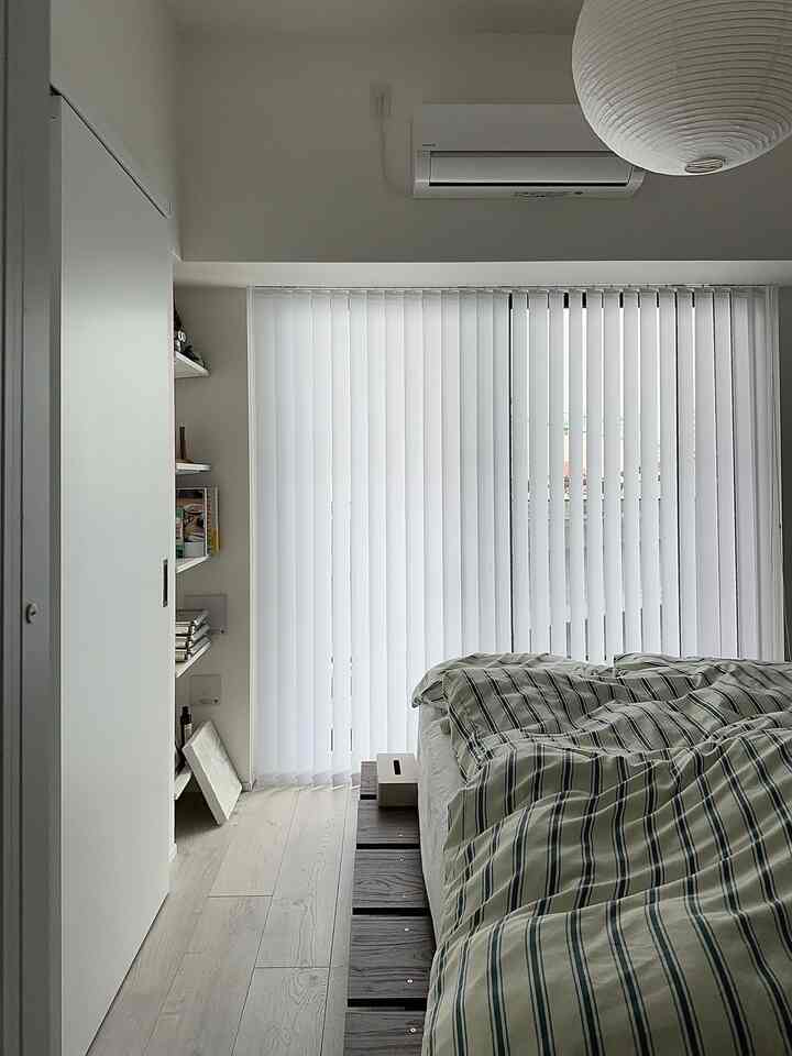 Natural modern bedroom with white and wood tones, featuring vertical blinds and patterned duvet cover in a cozy setting