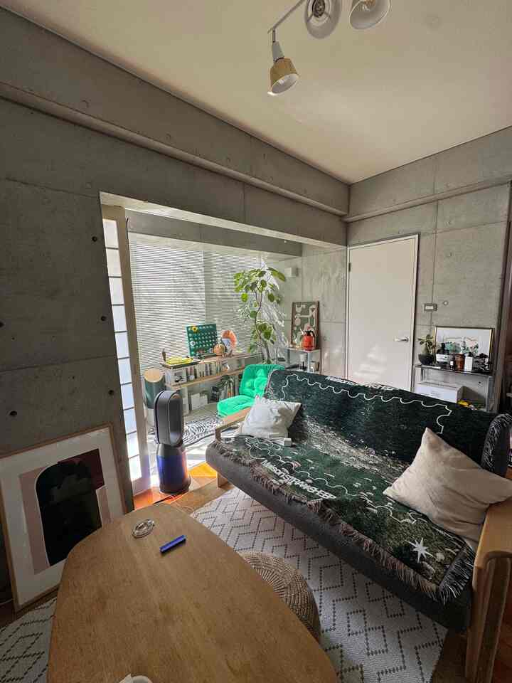 ナチュラルな色調とグリーンの家具が配置されたコンパクトなリビング、窓際に大きな植物がある印象的な空間