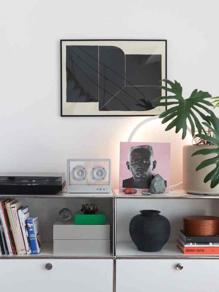 白い壁とモダンな棚にポスター、スピーカー、LPプレーヤー、花瓶、植物が配置された印象的な空間