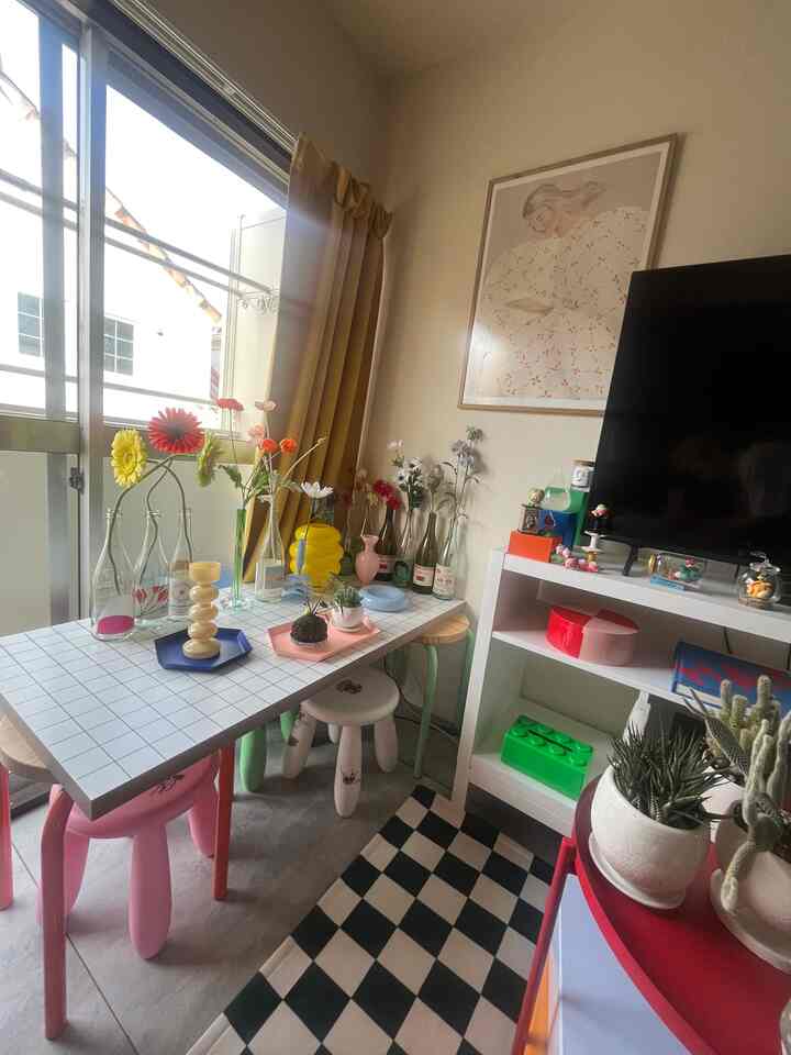 黄色いカーテンと白い家具が調和する狭くてコンパクトなバルコニー、花瓶と色とりどりの花が置かれたテーブルとスツールが囲む雰囲気のあるインテリア