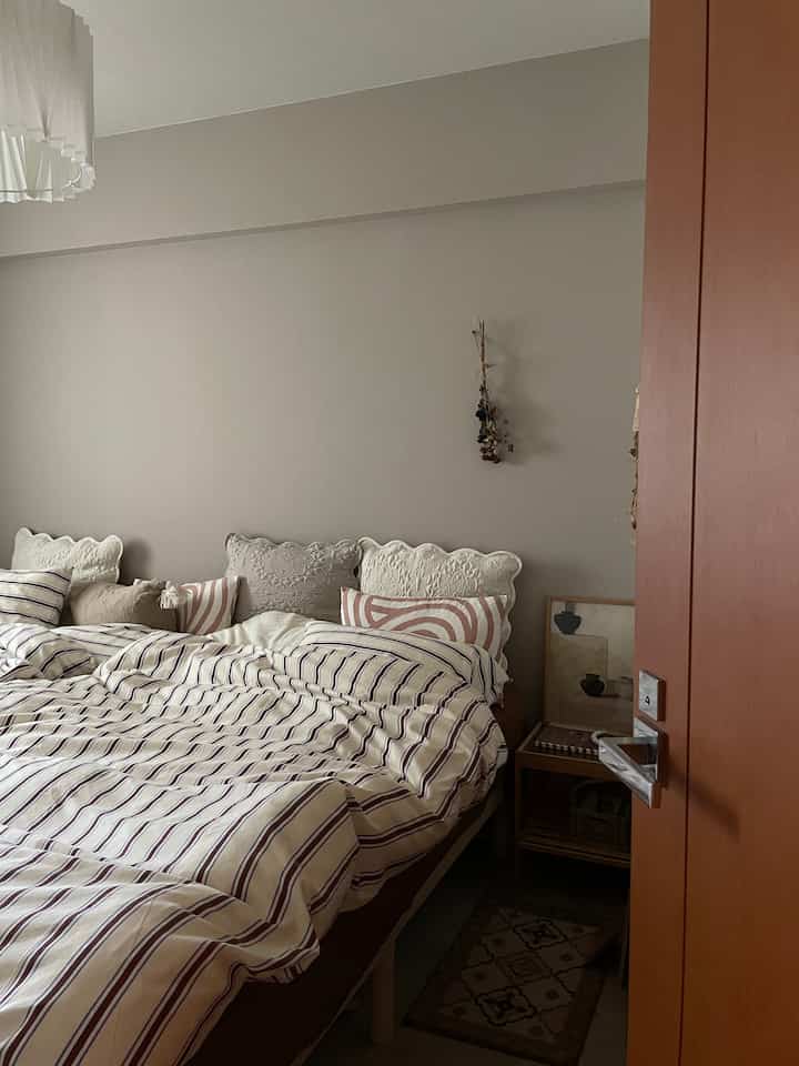 ナチュラルな色調の狭い6畳寝室、木目調のベッドとナイトテーブル、柄付き寝具が配置された印象的な空間