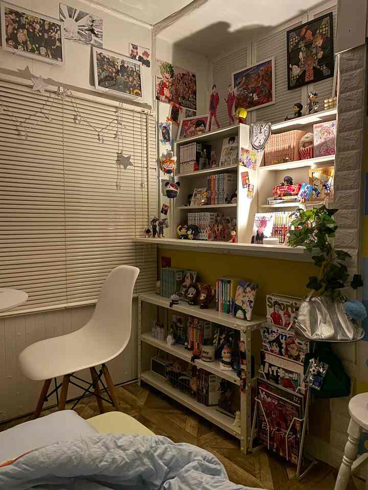 A cozy small 3-tatami manga room in white and yellow tones, with bookshelves and manga figurines filling the right wall