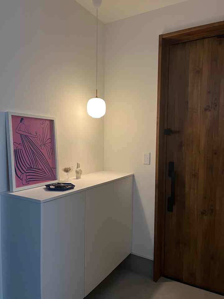 ホワイトと木目調が調和した玄関、ペンダントライトとポスターが配置された雰囲気のあるモダンなインテリア