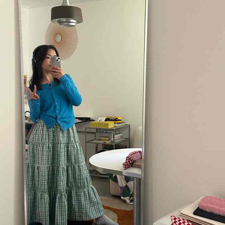 白い壁と天井のミッドセンチュリーモダンのリビングルームに、青いカーディガンを着た人物が全身鏡の前に立っている