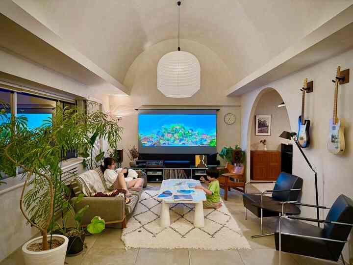 明るいホワイトトーンと自然なグリーン植物が調和したリビング、中央にソファと低いテーブルがあり、子供たちが過ごす居心地の良い空間