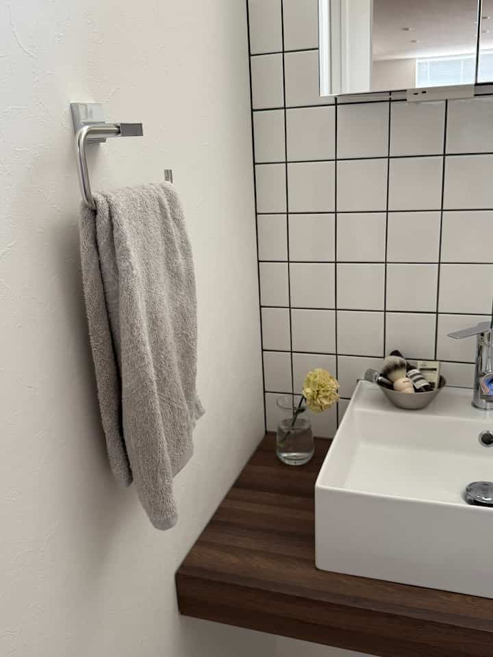 白と茶色のトーンのバスルーム、洗面台と鏡、タオルが配置されたシンプルでナチュラルな雰囲気のインテリア