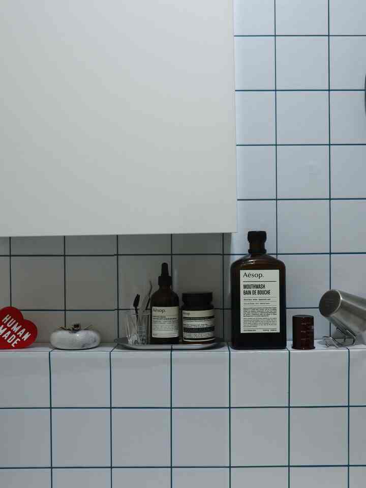 Minimalist bathroom shelf with white tiles and blue grid lines, featuring neatly arranged Aesop products creating a clean atmosphere