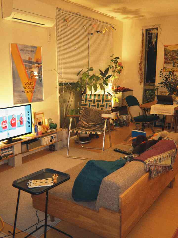 温かみのあるウッド調と観葉植物が配置された1LDKリビング、ミッドセンチュリーモダンのソファとダイニングテーブルがある雰囲気の良い空間