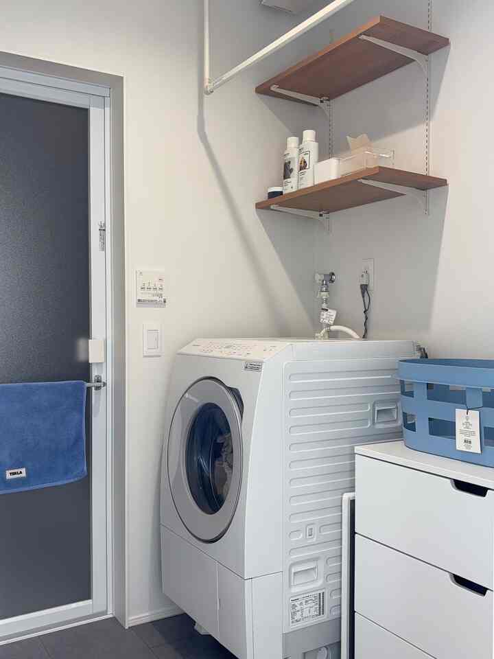 White and wood-tone shelves with a washing machine and storage cabinet in a clean compact laundry bathroom space