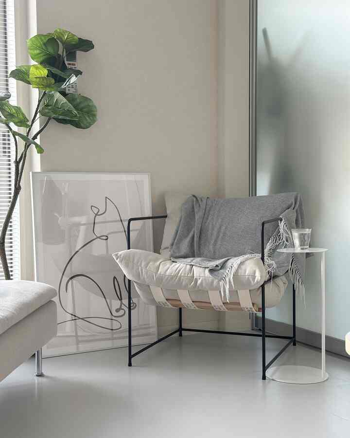 白とベージュの色調のリビング、黒いフレームのアームチェアとサイドテーブル、緑の植物が配されたシンプルでナチュラルなインテリア