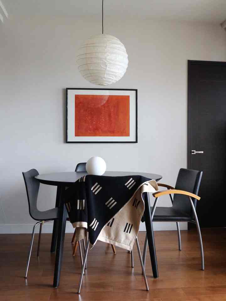 モノトーンとブラウンの床が調和するダイニング、黒の丸テーブルと椅子、白のペンダントライトが印象的な空間