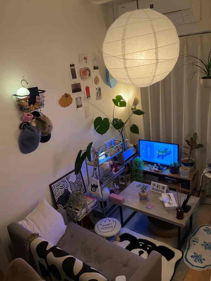 白を基調とした小さなリビング、グレーのソファとコーヒーテーブル、モニターと植物が配置されたモダンな空間