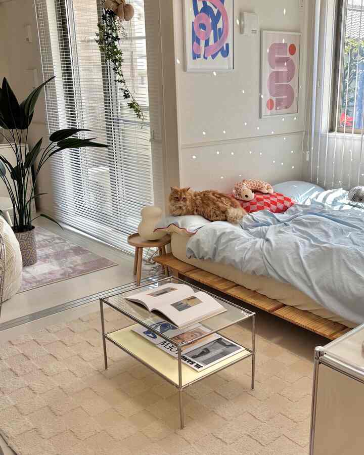 ホワイトとベージュ調の寝室、透明なガラステーブルとベッドの上の猫、植物が配置された雰囲気のある空間