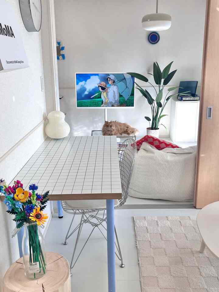 ホワイトトーンの狭い一人暮らし空間、くつろぐ猫とテーブル、フロアランプが配置された居心地の良いおうちカフェの雰囲気