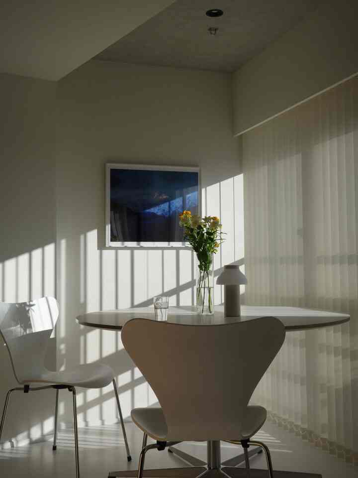 白を基調としたダイニング、北欧スタイルの椅子と丸テーブル、テーブルの上には花瓶とテーブルランプが置かれた清潔感のあるインテリア