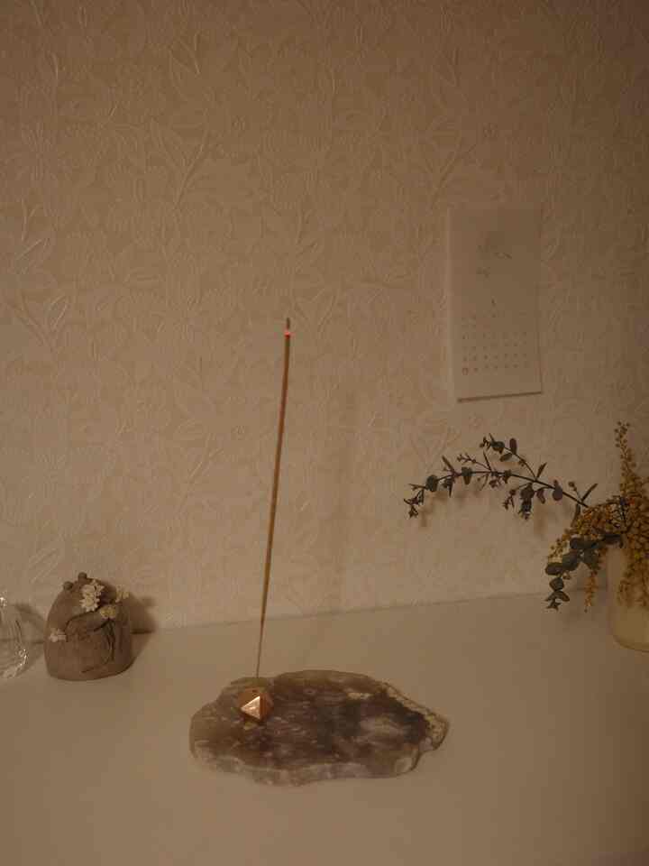 ベージュの壁紙と自然素材が調和したテーブル上に、真鍮のお香立てとドライフラワーが配置された雰囲気のある空間